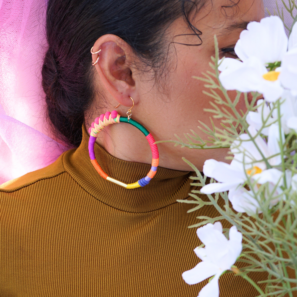 Model showcasing Brave hoop earrings, accentuating their vibrant and colourful design with pink pompom wrapped in peach and yellow thread, and gold plate accents.