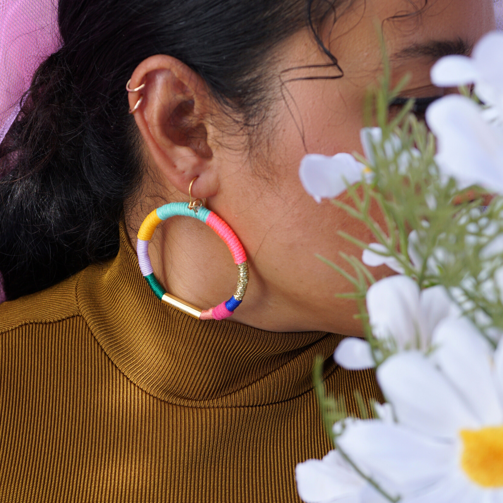 Model wearing a colorful hoop earring wrapped in vibrant thread with gold-tone accents. 