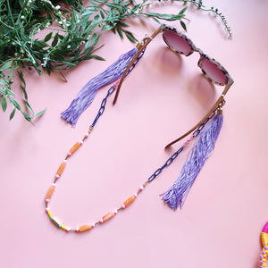 A stylish and multifunctional accessory that can be worn as a sunglasses chain, necklace, or lanyard. Featuring a mix of navy blue chain links, delicate colourful beads, and long flowing purple fringe for a bold and playful touch.