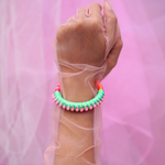 A fun and colorful bracelet designed with delicate pink pom-poms, intricate thread details, and a playful charm