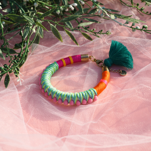 A fun and colourful bracelet designed with delicate pink pom-poms, intricate thread details, and a playful tassel charm