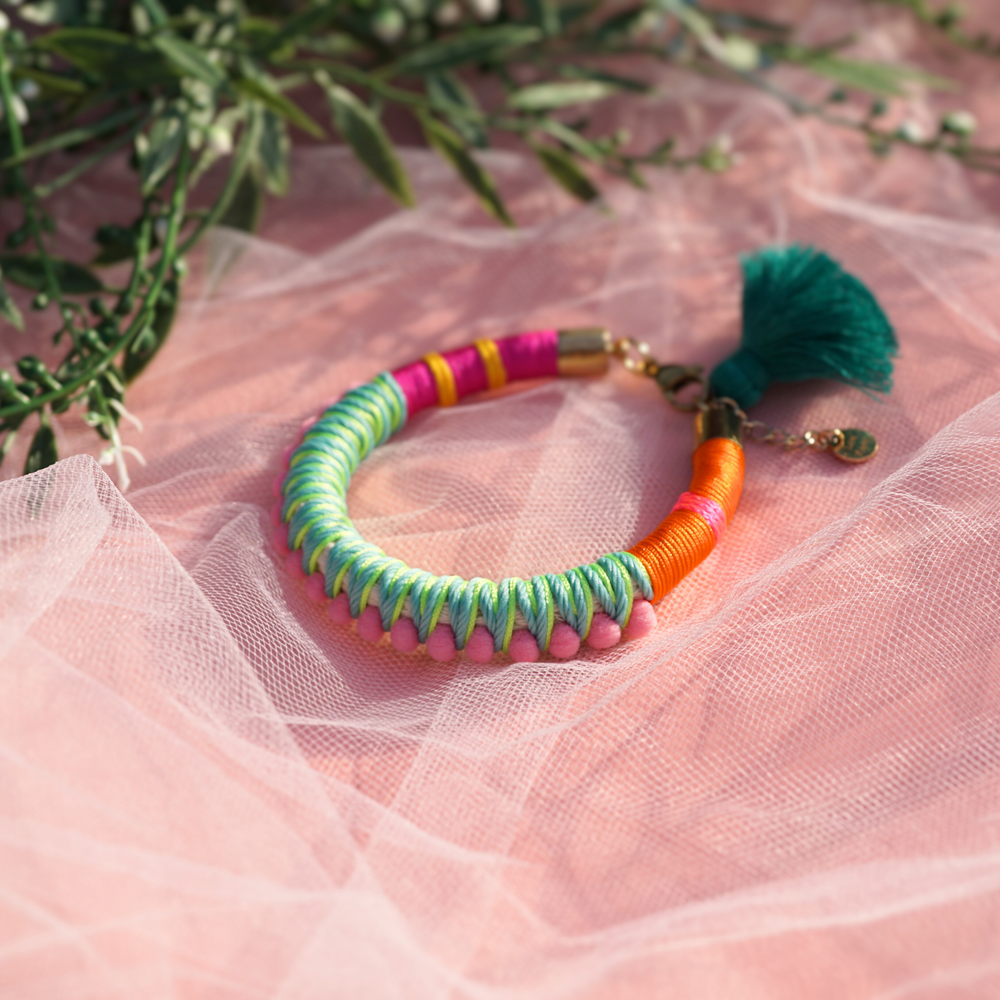 A fun and colourful bracelet designed with delicate pink pom-poms, intricate thread details, and a playful tassel charm