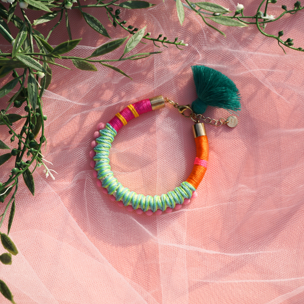 A fun and colourful bracelet designed with delicate pink pom-poms, intricate thread details, and a playful tassel charm