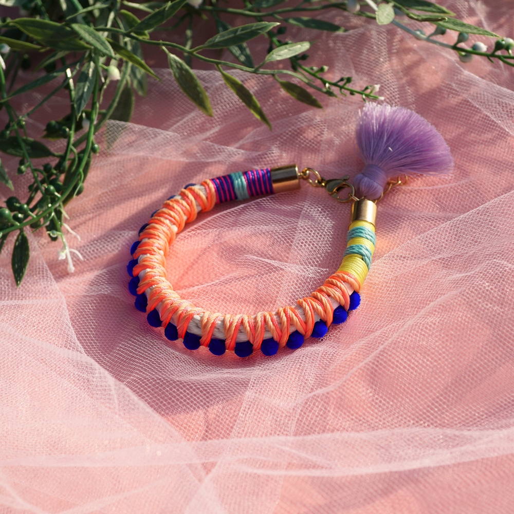 Vibrant statement bracelet featuring multicoloured thread, bold blue pom-poms, and a playful tassel charm