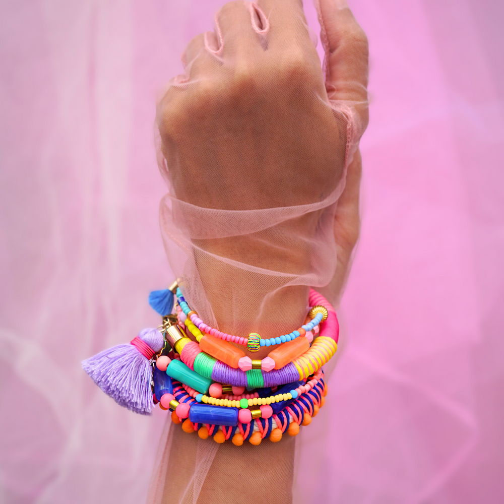 Vibrant statement bracelet featuring multicoloured thread, bold blue pom-poms, and a playful tassel charm