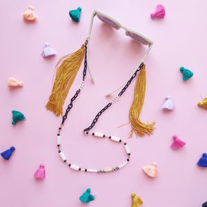 A stylish and multifunctional accessory that can be worn as a sunglasses chain, necklace, or lanyard. Featuring a mix of black and white links, delicate beads, and long flowing fringe for a bold and playful touch