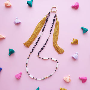 A stylish and multifunctional accessory that can be worn as a sunglasses chain, necklace, or lanyard. Featuring a mix of black and white links, delicate beads, and long flowing fringe for a bold and playful touch