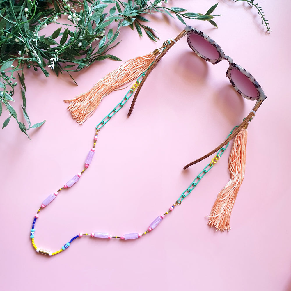 A stylish and multifunctional accessory that can be worn as a sunglasses chain, necklace, or lanyard. Featuring a mix of green and yellow chain links, delicate colourful beads, and long flowing peach fringe for a bold and playful touch.