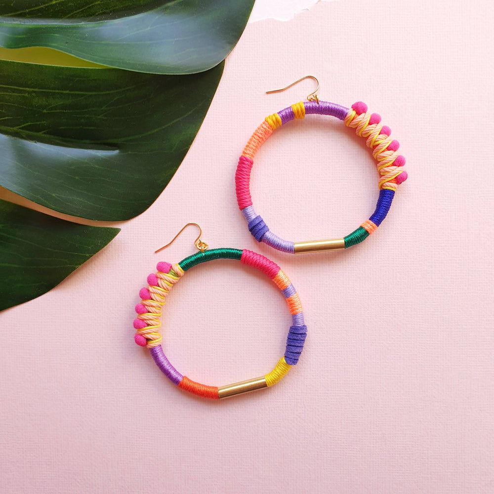 Colourful and vibrant hoop earrings with pink pompom wrapped in peach and yellow thread, accented with gold plate.