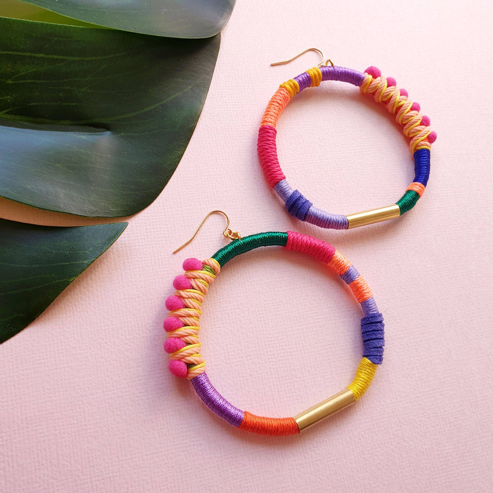 Colourful and vibrant hoop earrings with pink pompom wrapped in peach and yellow thread, accented with gold plate.