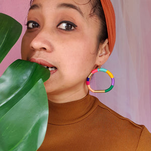 Model wearing a colorful hoop earring wrapped in vibrant thread with gold-tone accents. 