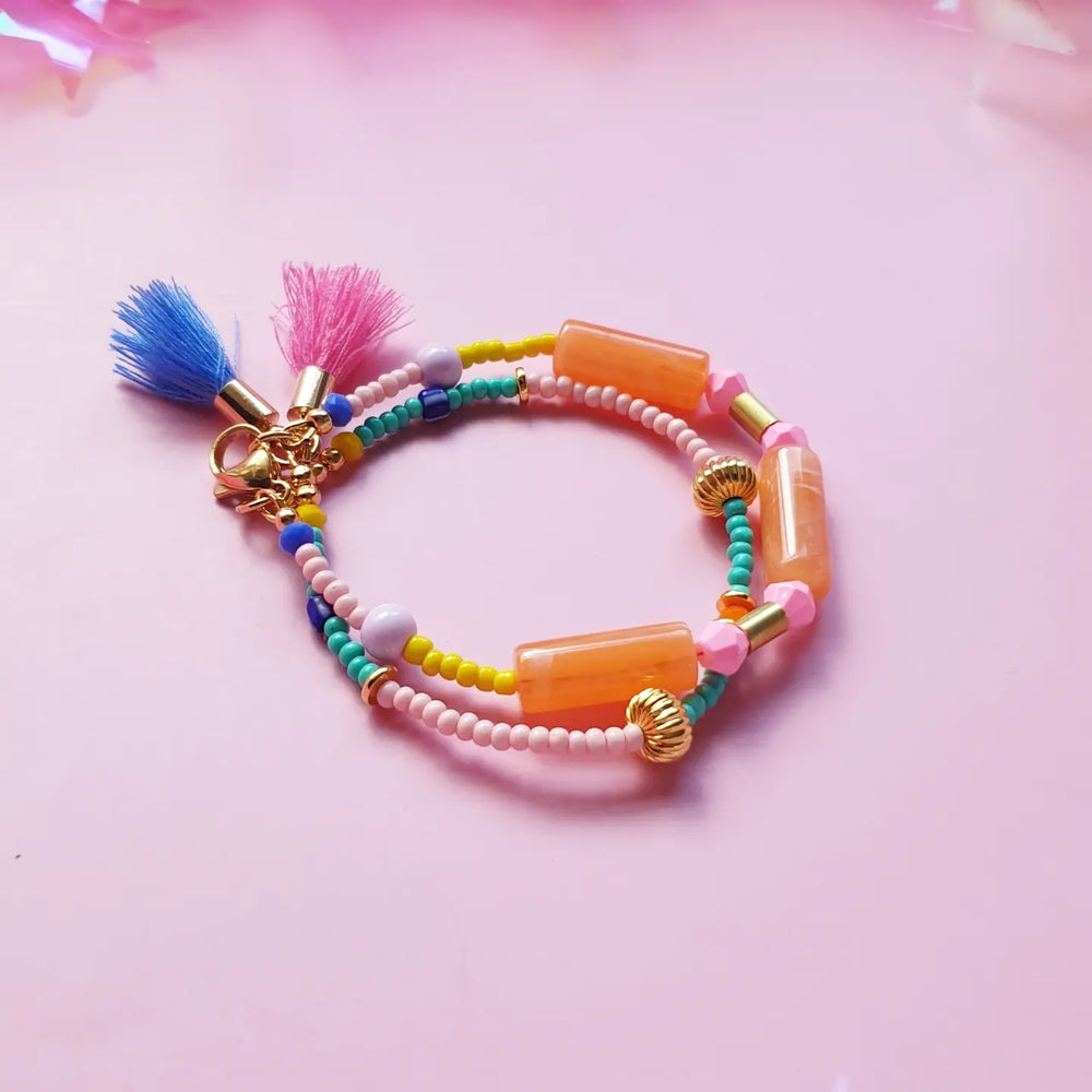 Beaded bracelet featuring orange resin tubes as the main accent, complemented by colourful beads and gold-plated round beads. Finished with tassels in random colours