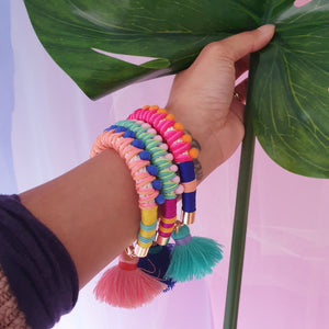 A model showcases vibrant and playful statement bracelets, featuring handwoven thread details, soft pom-poms, and a unique charm for an extra touch of fun