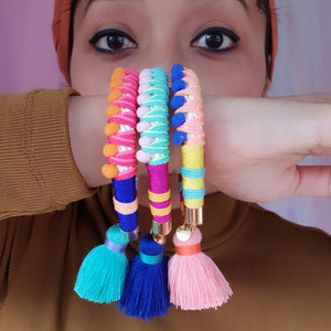 A model showcases vibrant and playful statement bracelets, featuring handwoven thread details, soft pom-poms, and a unique charm for an extra touch of fun