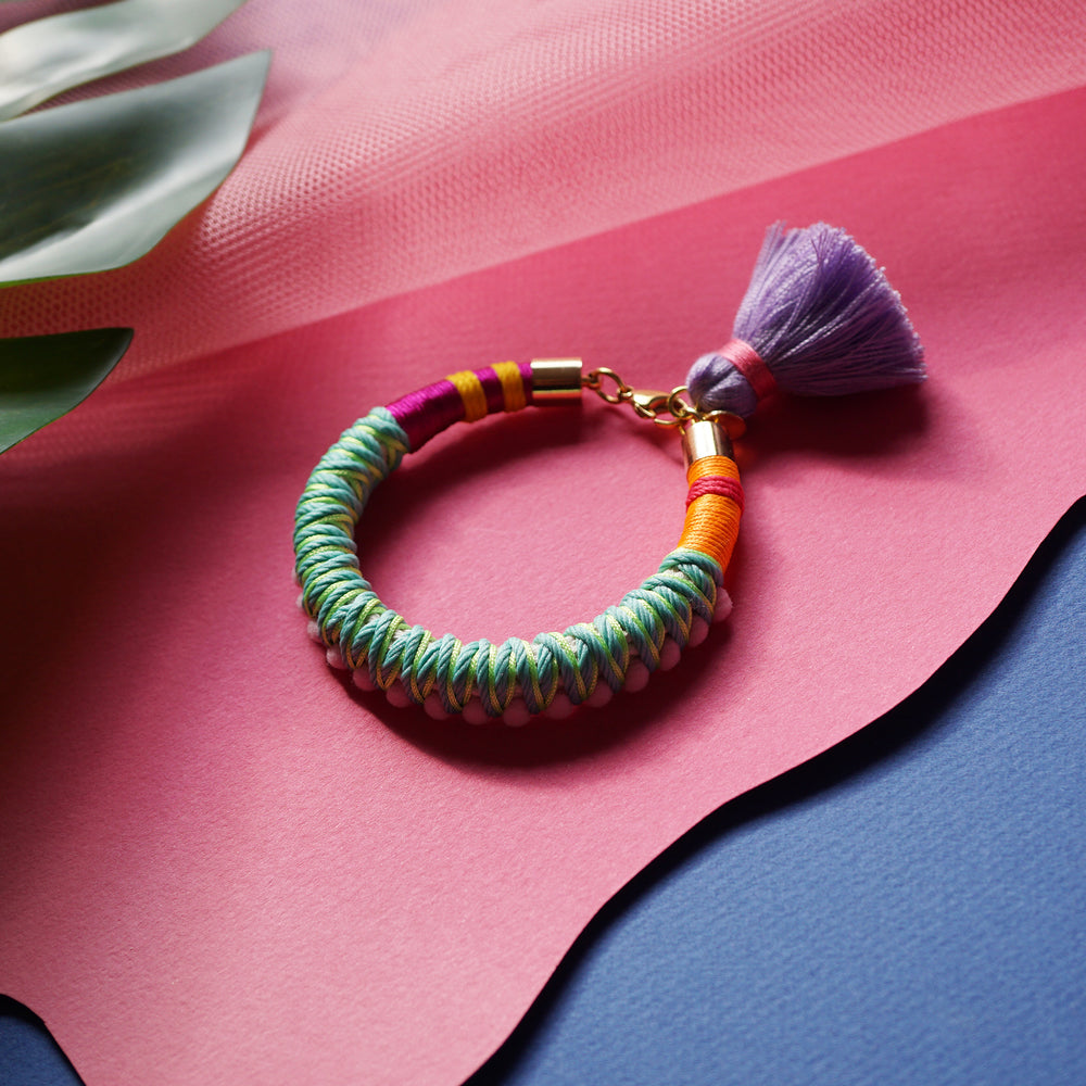 A fun and colourful bracelet designed with delicate pink pom-poms, intricate thread details, and a playful tassel charm