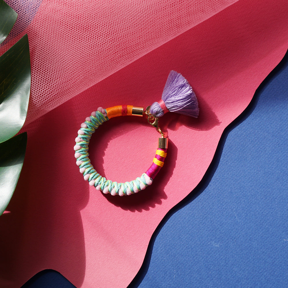 A fun and colorful bracelet designed with delicate pink pom-poms, intricate thread details, and a playful charm