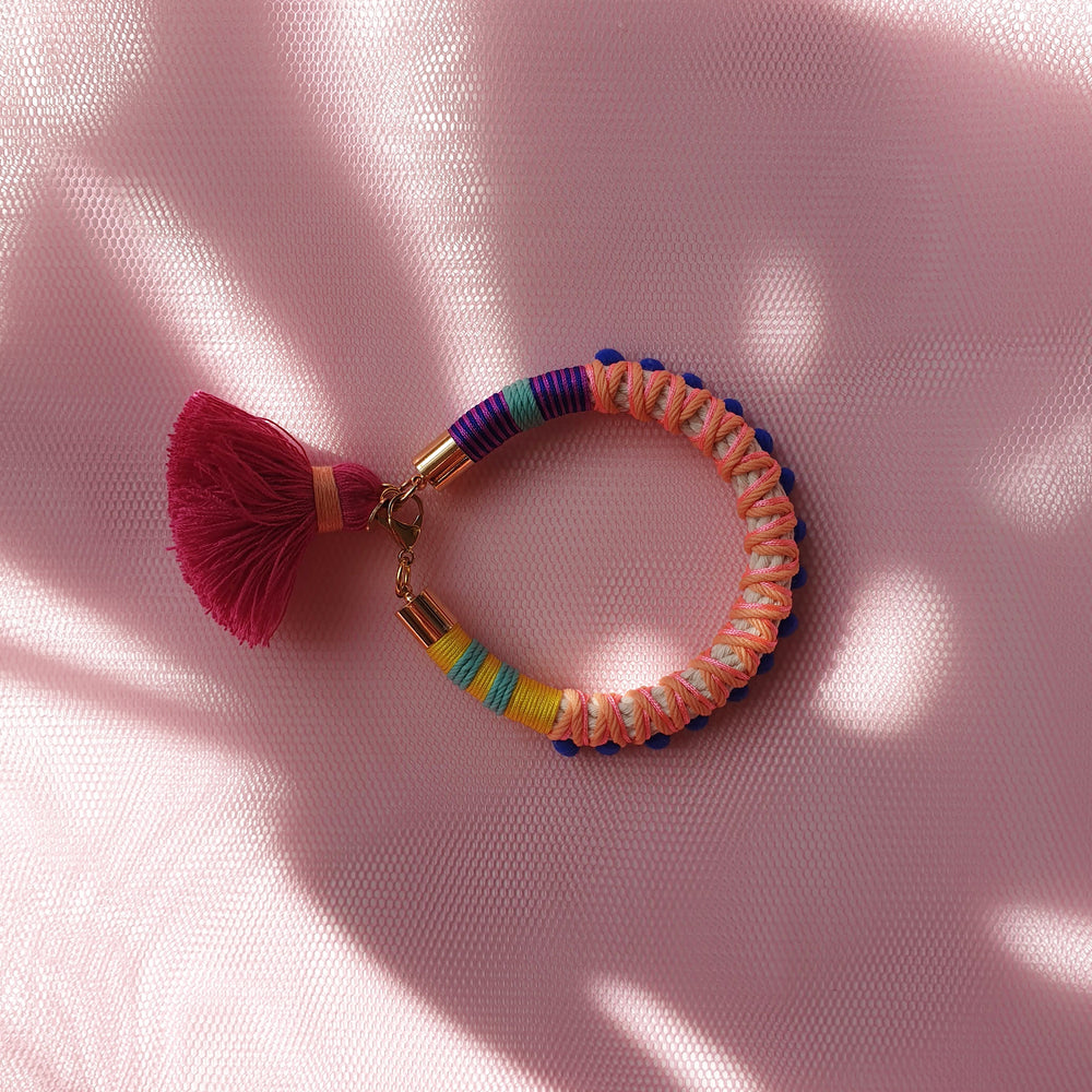 Vibrant statement bracelet featuring multicoloured thread, bold blue pom-poms, and a playful tassel charm.