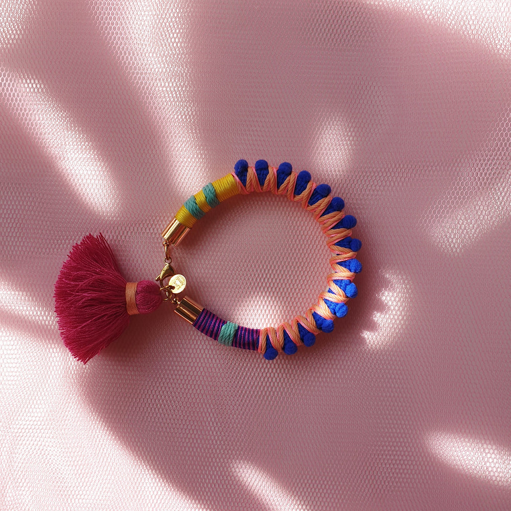 Vibrant statement bracelet featuring multicoloured thread, bold blue pom-poms, and a playful tassel charm