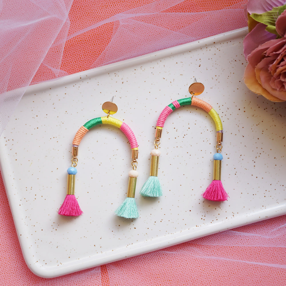 Arch-shaped earrings wrapped in colourful pastel threads featuring hand-dyed pink and mint tassels at each end.