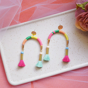 Arch-shaped earrings wrapped in colourful pastel threads featuring hand-dyed pink and mint tassels at each end.