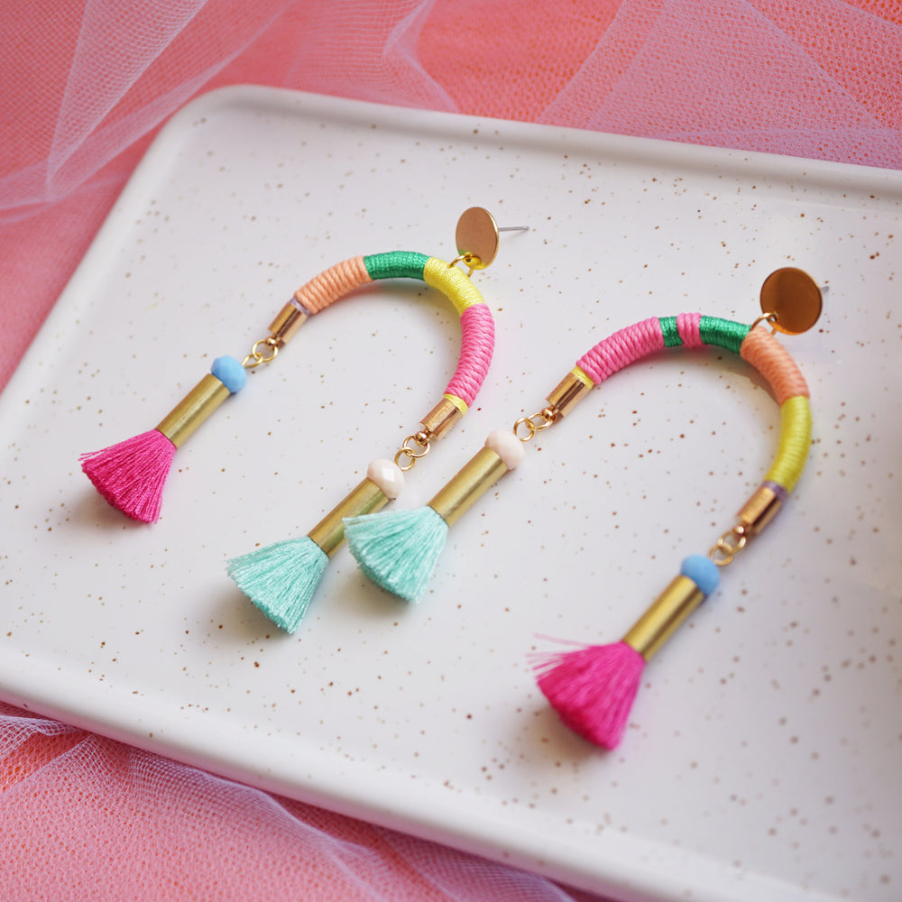 Arch-shaped earrings wrapped in colourful pastel threads featuring hand-dyed pink and mint tassels at each end.