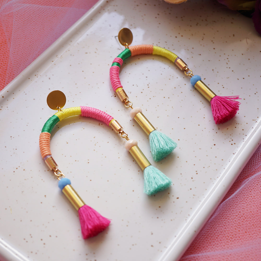 Arch-shaped earrings wrapped in colourful pastel threads featuring hand-dyed pink and mint tassels at each end.