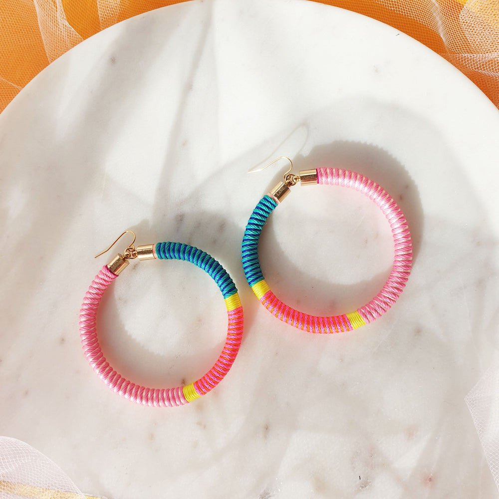 Model is wearing hoop earrings featuring a beautiful combination of pink, green, and yellow pastel colours for a soft, colourful look.