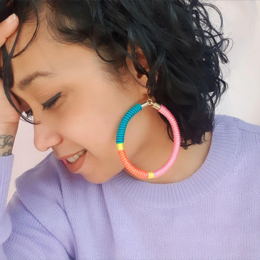 Model is wearing hoop earrings featuring a beautiful combination of pink, green, and yellow pastel colours for a soft, colourful look.