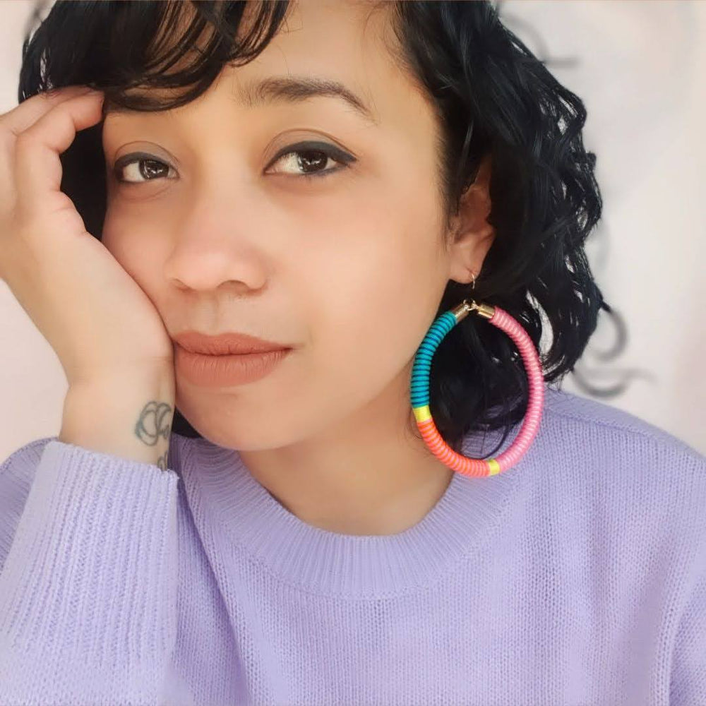 Model is wearing hoop earrings featuring a beautiful combination of pink, green, and yellow pastel colours for a soft, colourful look.