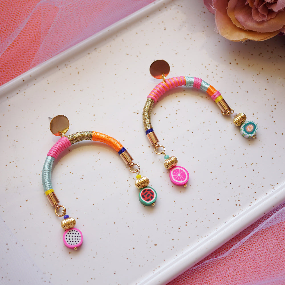 Colourful arch-shaped earrings with gold, pink, blue, and orange threads, gold-plated beads, and fruity beads at each end.